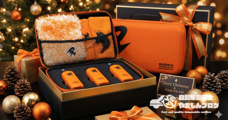 リボンで華やかにラッピングされたBUDDICA PHOENIX メンテナンスキットのギフトイメージ。洗車好きへの特別なプレゼントとして最適な、高級感あるオレンジ色の専用ハードケースとボトル。